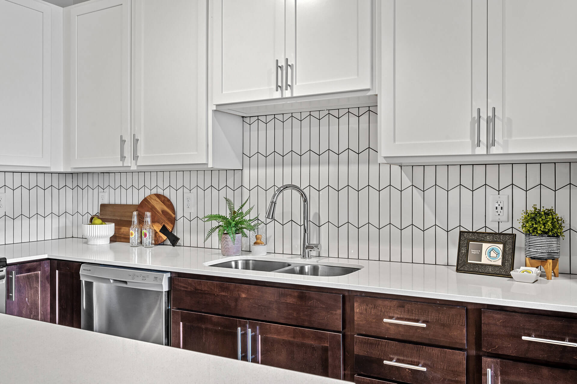 A close-up of a kitchen area with white quartz countertops, white shaker cabinets, dark wooden lower cabinets, stainless steel dishwasher, and a deep double sink.